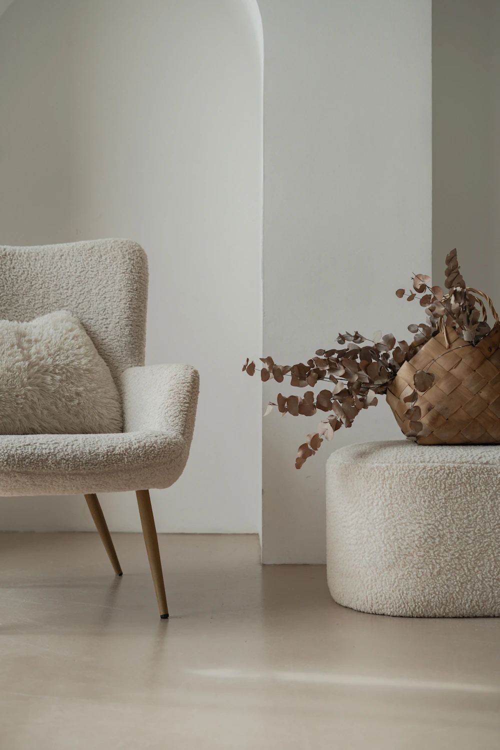 A cream bouclé armchair beside a vase of dried branches